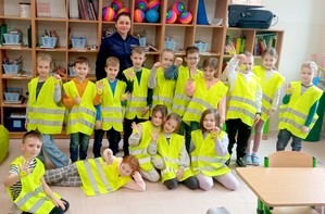 Zdjęcie grupowe z policjantką. Dzieci w żółtych kamizelkach odblaskowych.