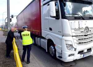 Policjantka w żółtej kamizelce odblaskowej prowadzi oględziny ciężarówki.
