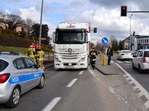 Ogólny widok na miejsce zdarzenia. W oddali ciągnik siodłowy z naczepą. Po lewej radiowóz policyjny. Widoczni strażacy i policjanci pracujący na miejscu zdarzenia.