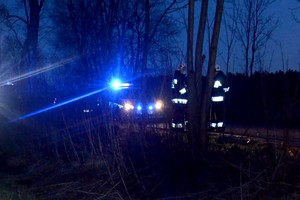 Stojący radiowóz z włączonymi światłami błyskowymi, a obok pracują służby.