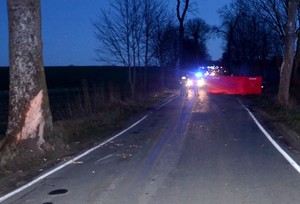 Pracujące na miejscu wypadku służby, radiowóz policyjny na światłach błyskowych oraz rozstawiony czerwony parawan straży pożarnej.