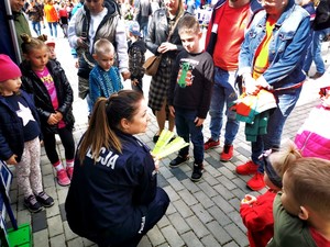 Policjantka w pozycji kucającej rozmawia z małymi dziećmi.