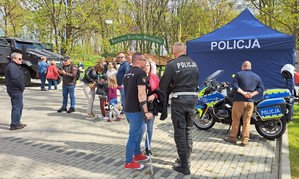 Ogólny widok na miejsce festynu. Widzimy policjanta z drogówki, motocykl służbowy oraz specjalistyczne auto kontr terrorystów z Gdańska. Pomiędzy liczne osoby przybyłe na festyn.