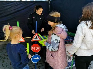 Policjantka w policyjnym namiocie wręcza dzieciom elementy odblaskowe.