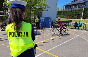 Policjantka w żółtej kamizelce odblaskowej nadzoruje przejazd rowerzysty na torze przeszkód.