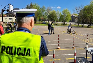 Policjant w żółtej kamizelce odblaskowej nadzoruje przejazd rowerzysty na torze przeszkód.