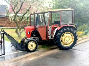 Traktor stojący przodem na uszkodzonym ogrodzeniu posesji.