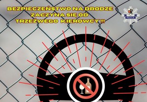 Grafika obrazkowa, siatka ogrodzeniowa,  kierownica ze znajdującym się w jej środkowej części alkoholem opisanym w znaku zakazu. Żółty napis: Bezepieczeństwo na drodze zaczyna się od trzeźwego kierowcy.