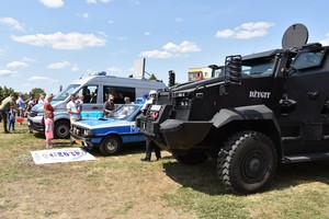 Zdjęcie z festynu, policjanci strażacy oraz dzieci. W tle namioty wystawowe dużo odwiedzających oraz sprzęt mundurowych.