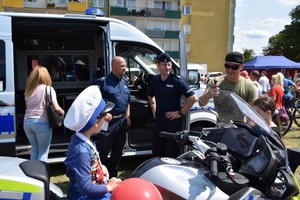 Zdjęcie z festynu, policjanci strażacy oraz dzieci. W tle namioty wystawowe dużo odwiedzających oraz sprzęt mundurowych.