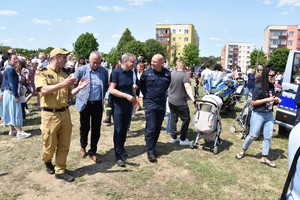 Zdjęcie z festynu, policjanci strażacy oraz dzieci. W tle namioty wystawowe dużo odwiedzających oraz sprzęt mundurowych.