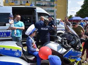 Ogólny widok na miejsce festynu. Dużo dorosłych, dzieci oraz sprzętu służbowego służb.