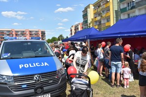 Ogólny widok na miejsce festynu. Dużo dorosłych, dzieci oraz sprzętu służbowego służb.