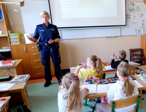 Policjantka w mundurze opowiada dzieciom siedzącym w klasie o bezpiecznych wakacjach.