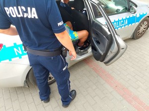 Policjant stoi przy otwartych tylnych drzwiach radiowozu przy siedzącym wewnątrz zatrzymanym nietrzeźwym kierowcy ciężarówki.