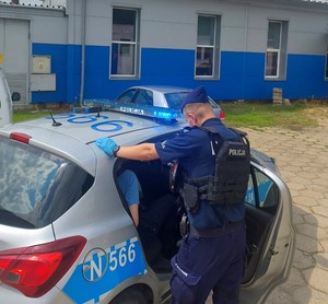 Radiowóz policyjny, przy którym stoi umundurowany policjant. W aucie siedzi zatrzymany kierowca.