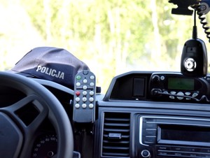 Widok z wnętrza radiowozu na przednią szybę. Na kokpicie po lewej stronie leży niebieska bejsbolówka z białym napisem o treści policja.