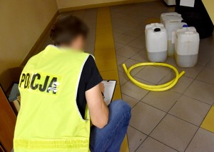 Policjant prowadzi oględziny zabezpieczonych plastikowych baniaków, w których znajduje się olej napędowy.