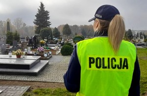 Policjantka w żółtej kamizelce odblaskowej stoi na cmentarzu.