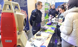 Policjanci na targach edukacyjnych EDU DAY stoją przy swoim punkcie informacyjnym i rozmawiają z maturzystami.