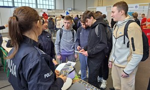 Policjanci na targach edukacyjnych EDU DAY stoją przy swoim punkcie informacyjnym i rozmawiają z maturzystami.