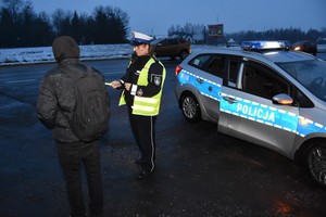 Ponury poranek. Pada deszcz. Policjantka wręcza pieszemu odblask.