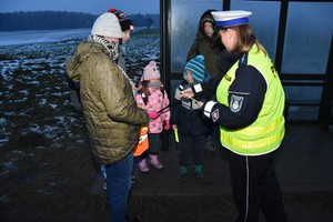 Ponury poranek. Pada deszcz. Policjantka wręcza pieszemu odblask.