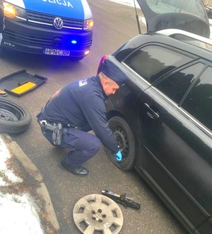 Policjant zmienia koło w aucie.