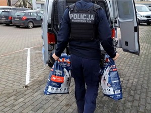 Policjant niesie do radiowozu 2 worki z karmą.