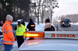 Członkowie komisji: policjanci, strażak oraz przedstawiciele Generalnej Dyrekcji Dróg Krajowych i Autostrad na miejscu wypadku drogowego. w czasie pracy. Na poboczu zaparkowane pojazdy służb uczestniczących w pracach komisji z włączonymi światłami błyskowymi.