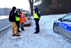 Członkowie komisji: policjanci, strażak oraz przedstawiciele Generalnej Dyrekcji Dróg Krajowych i Autostrad na miejscu wypadku drogowego. w czasie pracy. Na poboczu zaparkowane pojazdy służb uczestniczących w pracach komisji z włączonymi światłami błyskowymi.