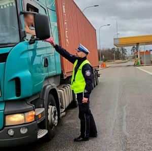 Policjant w czasie kontroli drogowej wręcza kierowcy apteczkę pierwszej pomocy.