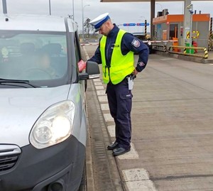 Policjant w czasie kontroli drogowej wręcza kierowcy apteczkę pierwszej pomocy.