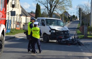 Policjanci pracują na miejscu zdarzenia. W tle rozbite pojazdy - VW Transporter i motocykl.