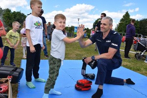 Policjant w przyklęku przybija tak zwaną piątkę chłopcu, który stoi z nim na macie treningowej.