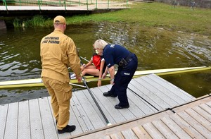 Policjantka ze strażakiem pomagają wysiąść kobiecie z kajaka.