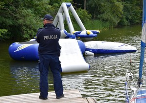 Policjant z pomostu spogląda na dmuchany tor przeszkód pływający na jeziorze.