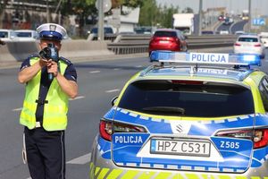 Policjant z miernikiem prędkości stoi obok radiowozu.