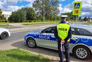 Policjant z drogówki nadzoruje ruch przy przejściu w pobliżu szkoły.