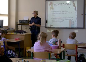 Policjantka w klasie przy tablicy opowiada dzieciom o bezpiecznej drodze do szkoły.