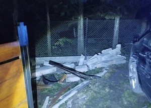 Po lewej stronie uszkodzony płot, a po prawej rozbite na płocie auto.