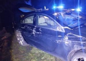 Rozbity opel, a w tle widoczne światła błyskowe radiowozów.