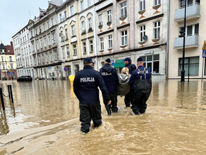 Policjanci stoją w wodzie na zalanej ulicy i pomagają powodzianom.