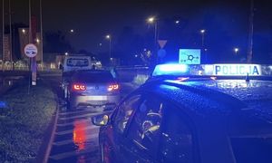 Radiowóz z włączonymi światłami błyskowymi stoi w nocy przed skrzyżowaniem o ruchu okrężnym.