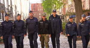 Grupa policjantów idzie w szeregu, całą szerokością jedną z ulic gdańskiej starówki.