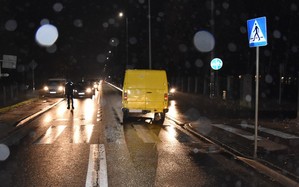 Policjanci zabezpieczają miejsce wypadku. Ciemno, mokra droga. Przejście dla pieszych oraz żółty dostawczy mercedes.