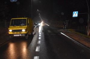 Policjanci zabezpieczają miejsce wypadku. Ciemno, mokra droga. Przejście dla pieszych oraz żółty dostawczy mercedes.