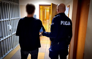 Policjant prowadzi zatrzymanego mężczyznę.