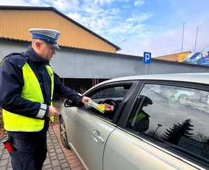 Policjant wręcza kierowcy latarkę.