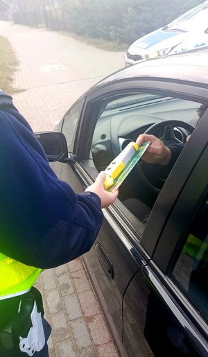 Policjant wręcza kierowcy latarkę.